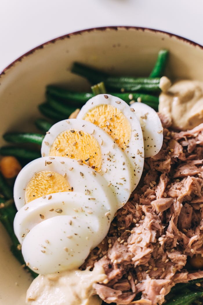 A fresh and nutritious tuna salad featuring sliced eggs, green beans, and seasoning, perfect for a healthy meal.